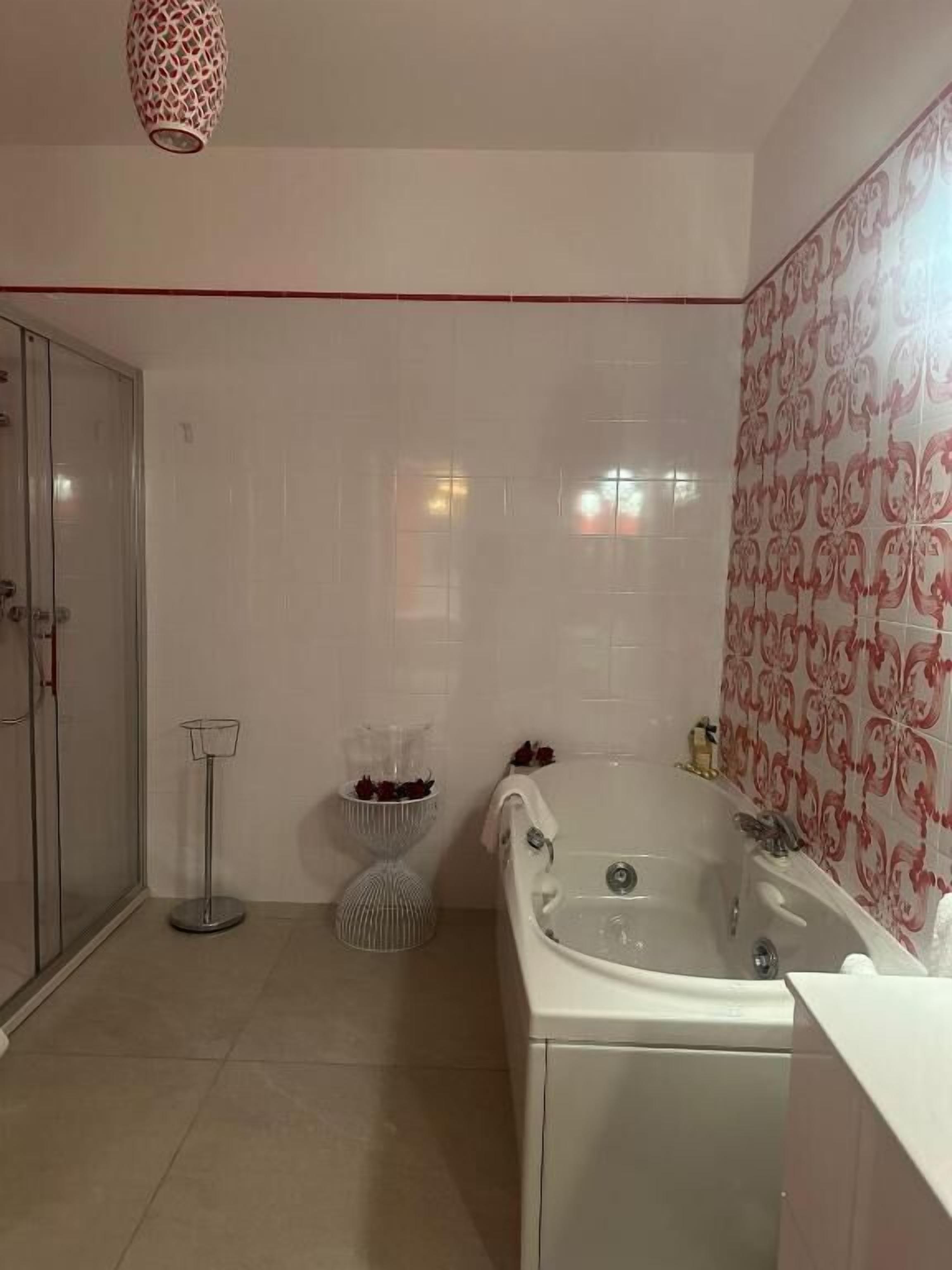 A bathroom with a bathtub, a shower, and a toilet. There is a towel rack and a small shelf with decorative items.