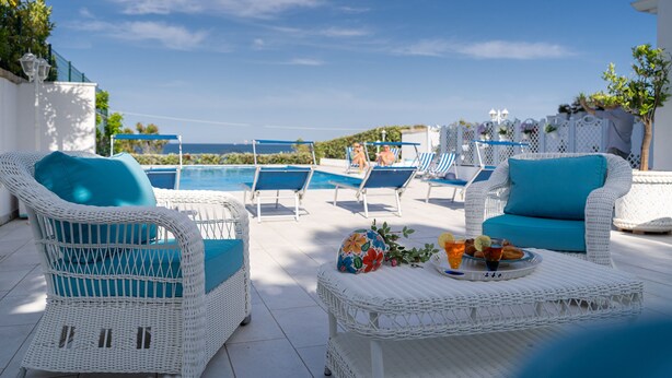 A poolside area with wicker furniture, a table with drinks, and a view of the sea. - Almare' (Crotone)