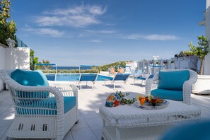 A poolside area with wicker furniture, a table with drinks, and a view of the sea.