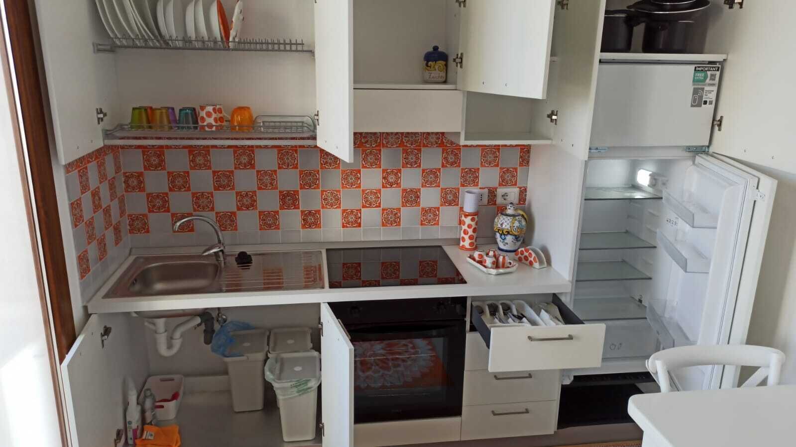 A compact kitchen with a sink, a stove, and a refrigerator. There are cabinets above the counter and a small countertop area.