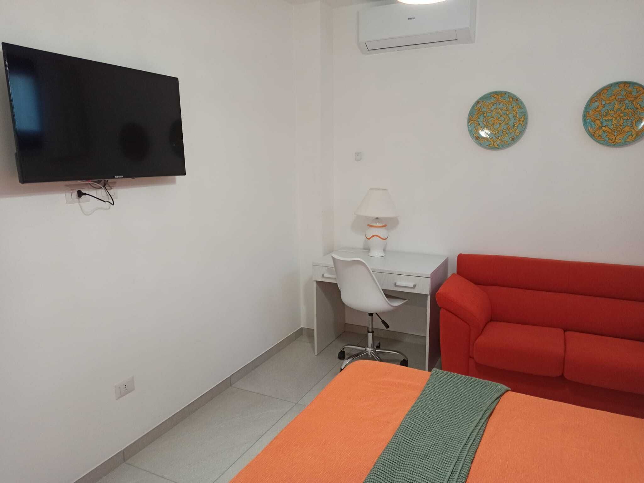 Een kamer met een bed, een bureau met stoel, een televisie en twee decoratieve borden aan de muur.
