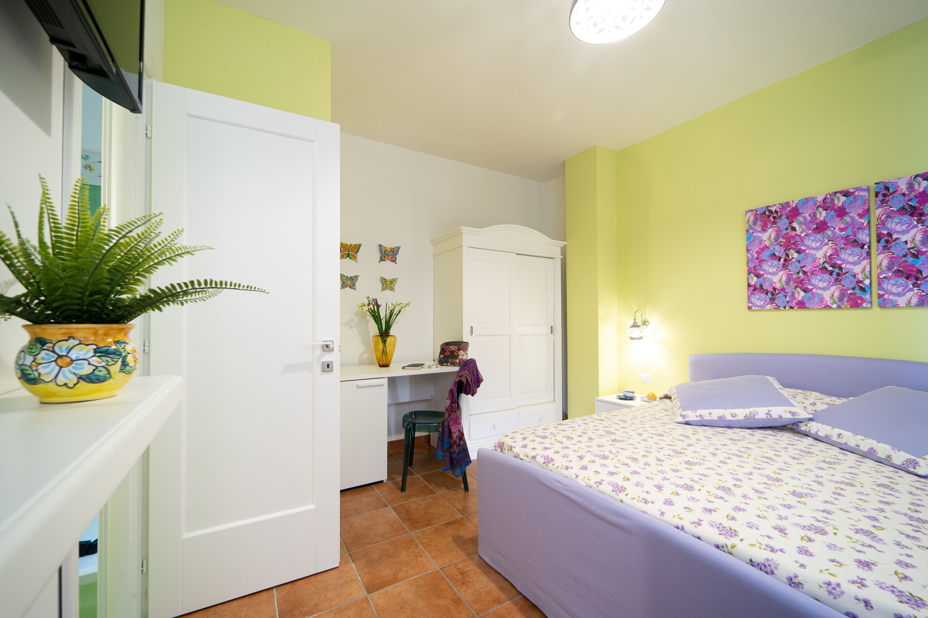 Une chambre à coucher comprenant un lit, un bureau, une chaise, une armoire, une plante en pot et un mur décoré d’autocollants représentant des papillons.