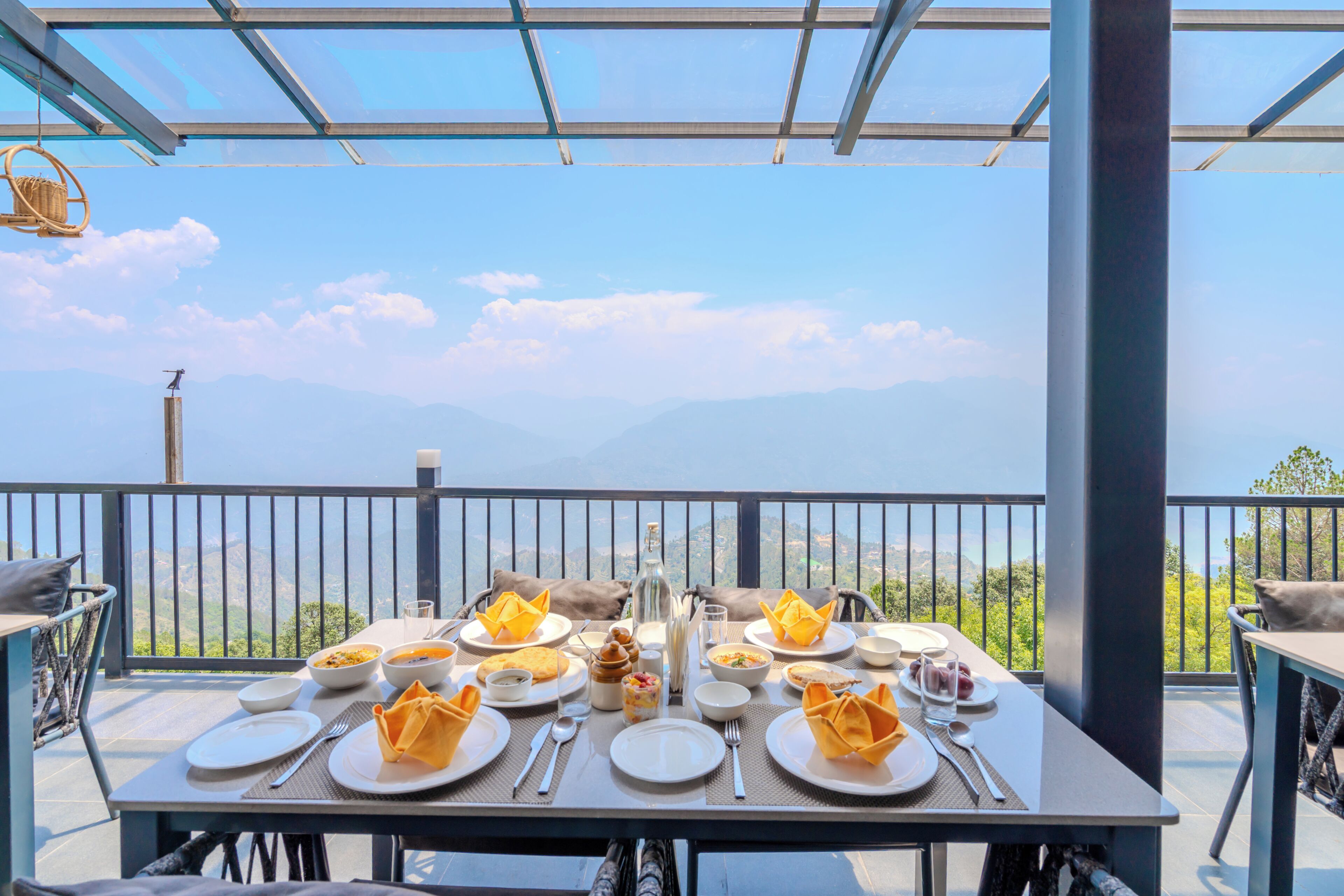 A table set for a meal with a view of mountains, a glass ceiling, and a railing.