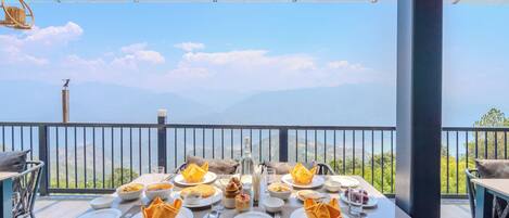 A table set for a meal with a view of mountains, a glass ceiling, and a railing.
