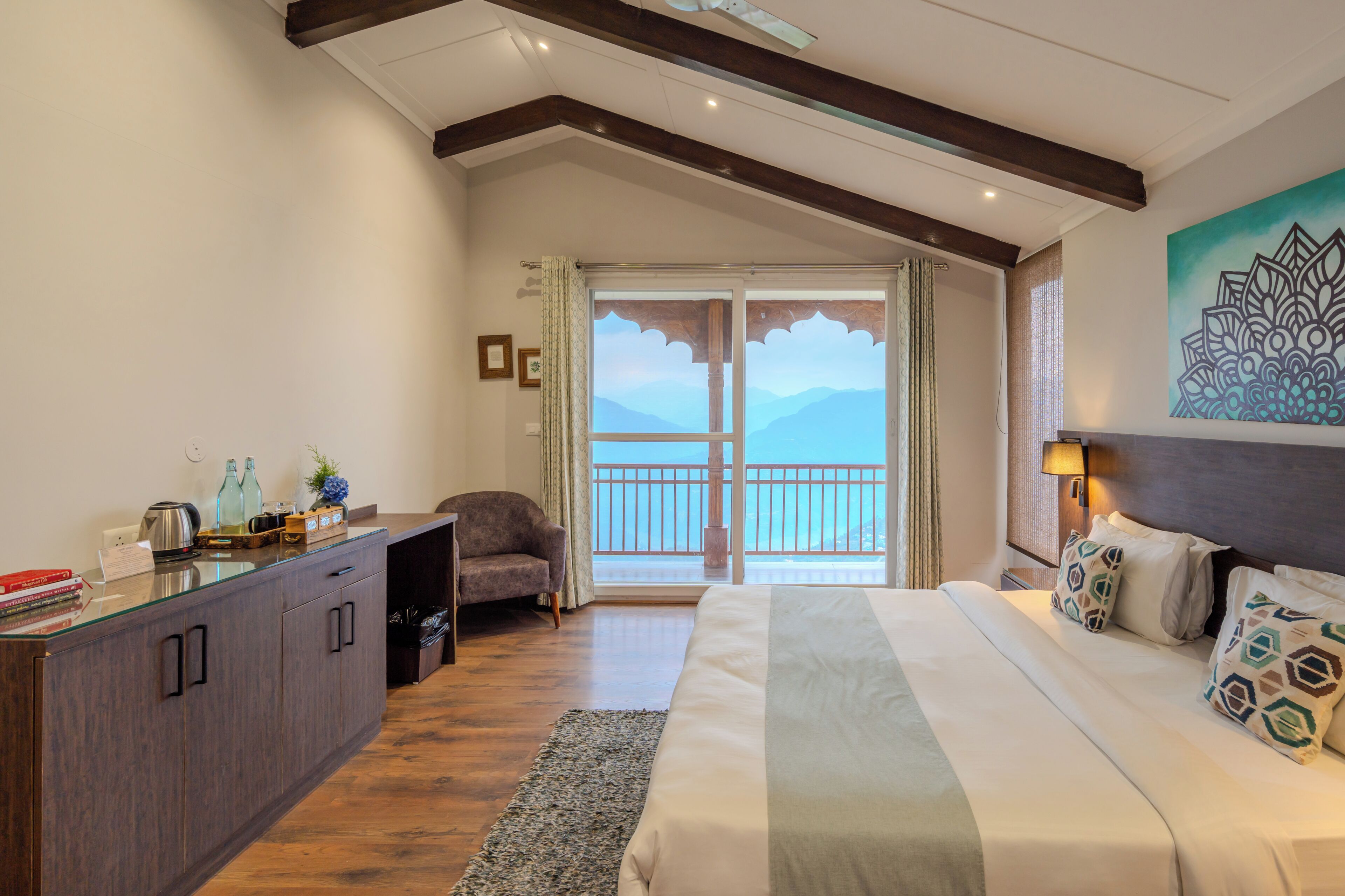 A bedroom with a bed, a desk, a chair, and a view of the mountains through the balcony doors.