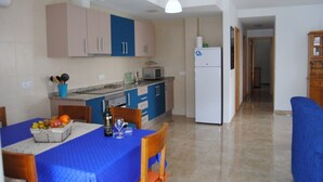 Cozinha compacta com área de refeições, incluindo geladeira, micro-ondas e mesa posta com frutas e uma garrafa.