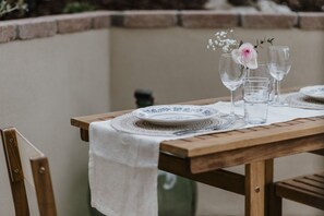 Una mesa de madera con mantel blanco, un plato y dos copas de vino con un arreglo floral.
