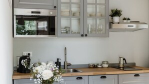 A modern kitchen with grey cabinets, a stainless steel oven, a coffee machine, and a sink.