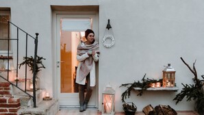 A person standing at a door with a white wall, a small shelf with candles, and a lantern.