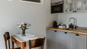 A kitchen with a wooden table, chairs, a vase of flowers, a coffee maker, and a sink.