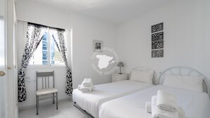 Ett hotellrum med två sängar, en stol, ett fönster med mönstrade gardiner, en tavla som hänger på väggen och en dekorativ väggdekoration.