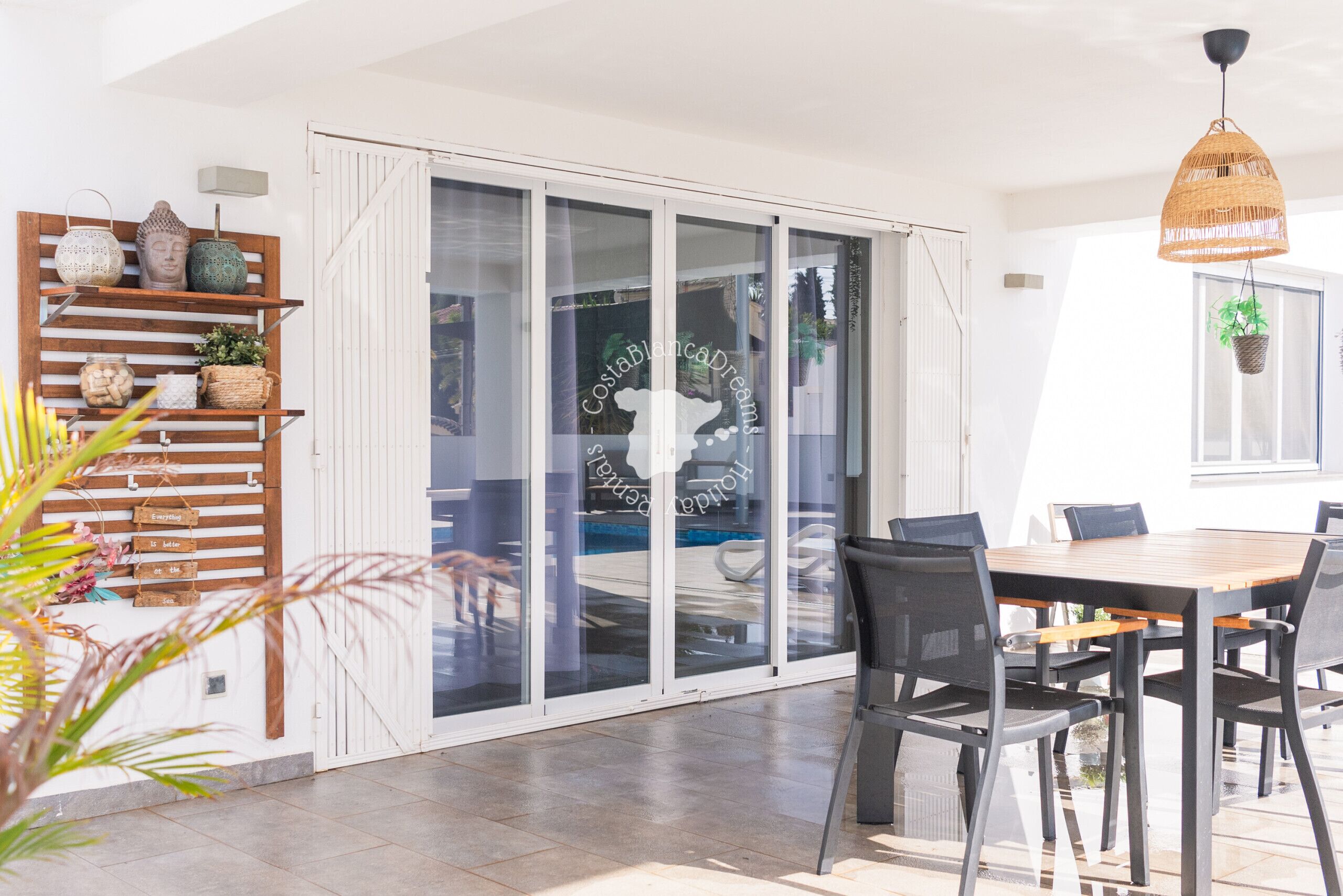 A modern dining area with a wooden table and chairs, a glass door leading outside, and a hanging wicker light fixture.