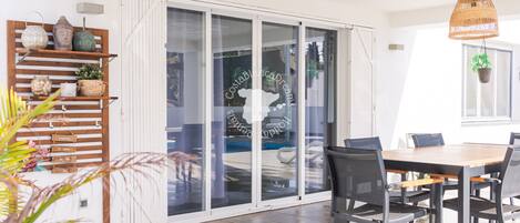 A modern dining area with a wooden table and chairs, a glass door leading outside, and a hanging wicker light fixture.