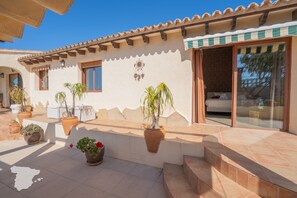 A building with a patio area, potted plants, and a sliding glass door leading to a bedroom.