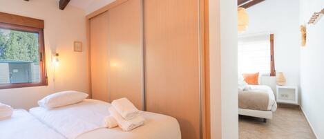 A bedroom with two beds, a sliding wooden door, a window with a view, and a bedside table with a lamp.