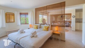 Un dormitorio amplio con una cama grande, mesitas de noche, un banco y vistas al exterior.