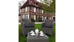 Un edificio tradicional de estilo Tudor con techo de paja y estructura de madera. En el frente, una mesa de mimbre con vajilla de té blanca y dos sillas de mimbre con cojines oscuros.