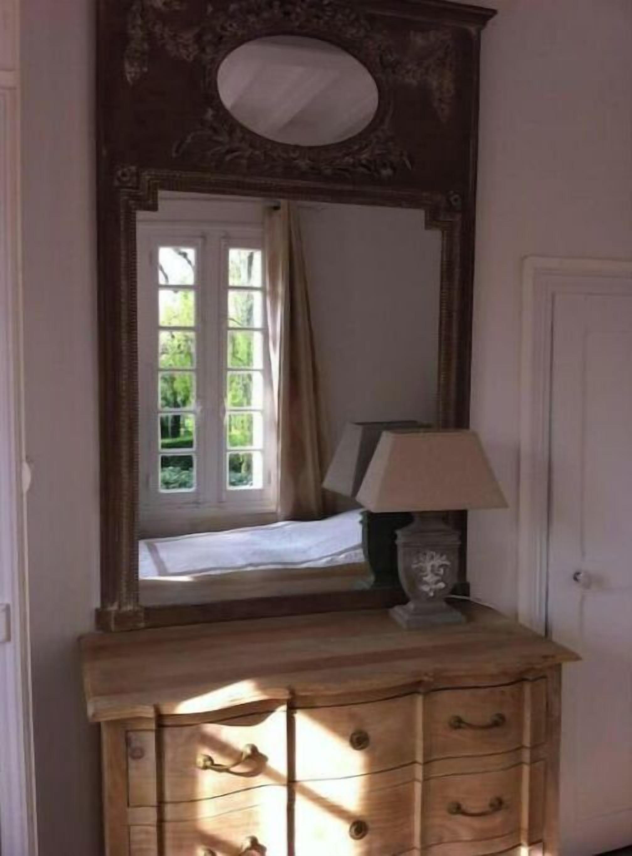 Un aparador de madera con un espejo encima, una lámpara en la parte superior y una ventana con cortinas.