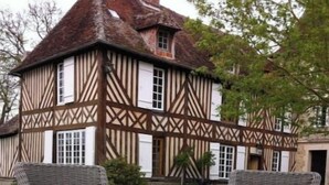 Un edificio tradicional de estilo Tudor con techo de paja y estructura de madera. En el frente, una mesa de mimbre con vajilla de té blanca y dos sillas de mimbre con cojines oscuros.