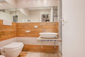 A modern bathroom with a white toilet, a vessel sink, and a glass shower enclosure. - Rialto Suite (Venice)