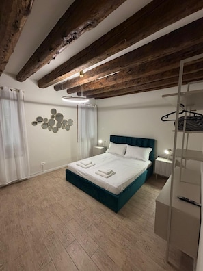 A bedroom with a bed, wooden beams, a wall-mounted light fixture, and a hanging light. - Rialto Suite (Venice)