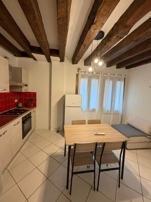 A compact kitchen with a dining table and chairs, a built-in oven, and a refrigerator. - Rialto Suite (Venice)