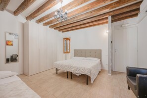 Quarto com cama, vigas de madeira, um candelabro, um espelho e uma porta.