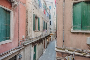 A narrow alleyway with buildings on either side, featuring exposed brickwork, green shutters, and visible electrical wiring. - Rialto Suite (Venice)
