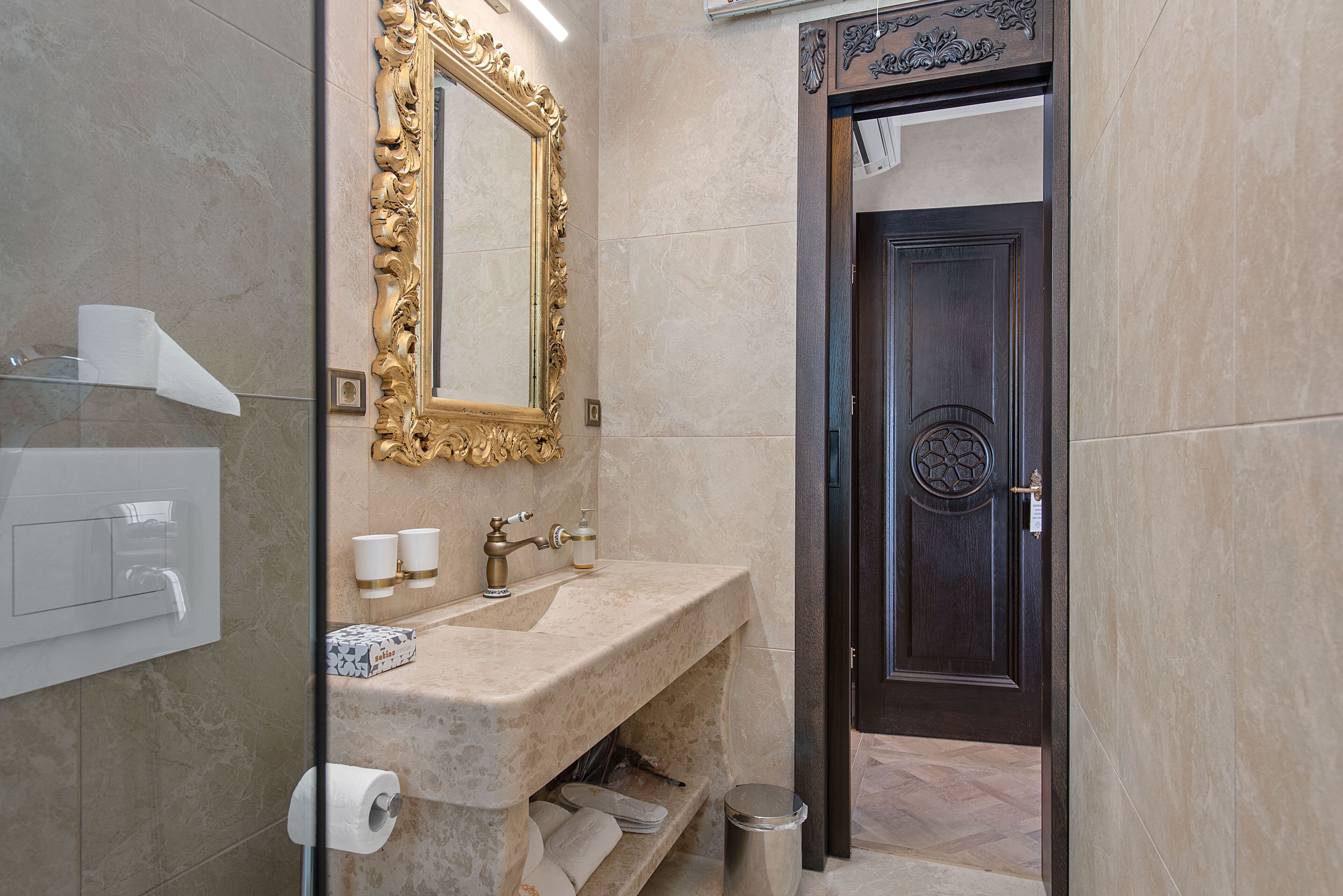 A bathroom with a marble sink, a gold-framed mirror, and a dark wooden door.