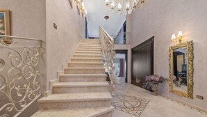 Una majestuosa escalera con barandales ornamentados, un candelabro y un espejo con marco dorado.