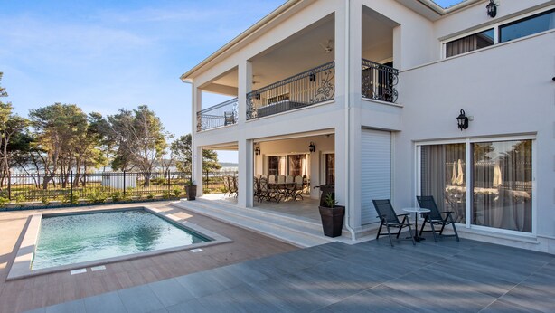 Una casa de dos plantas con piscina, mobiliario exterior y vista al mar.