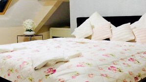 A neatly made bed with a floral bedspread, a bedside table with a vase of flowers, and a headboard with multiple pillows. - Apartment in Gammertingen With Terrace (Gammertingen)