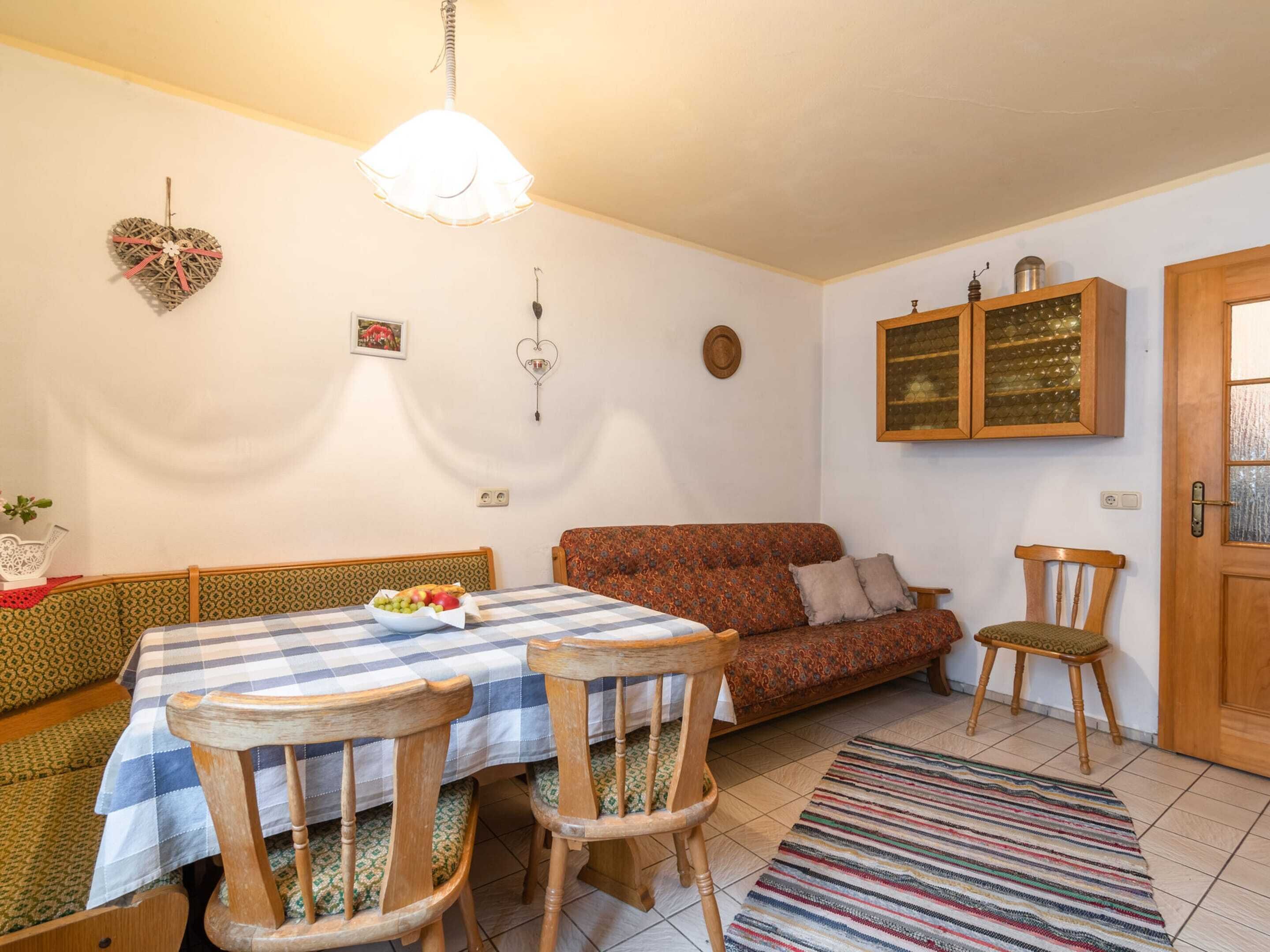 A cozy living room with a dining table, two wooden chairs, a sofa, and a patterned rug.