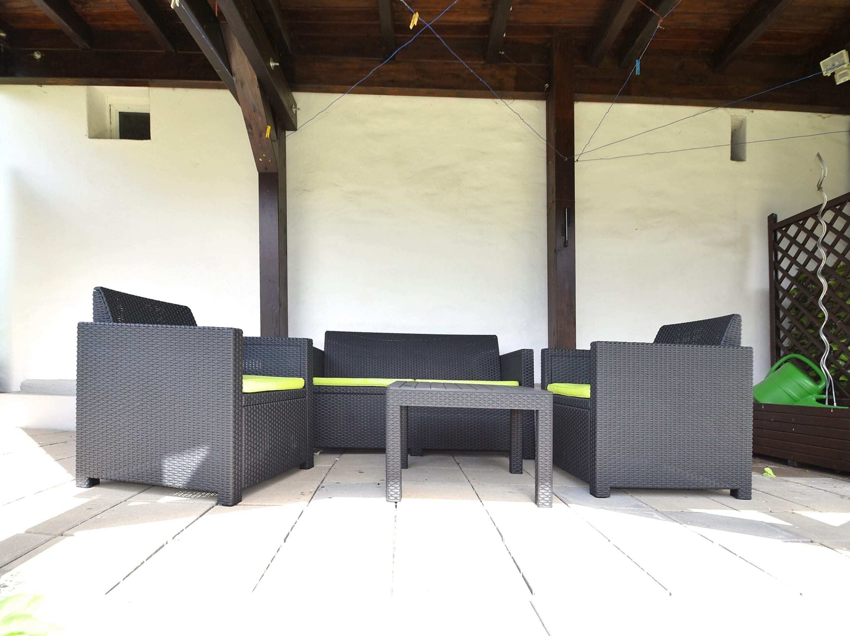 A covered patio area with a dark wicker sofa set and a small table.