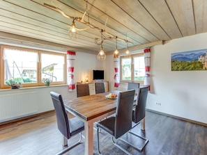 Un coin repas avec une table en bois, six chaises et un téléviseur posé sur un meuble.
