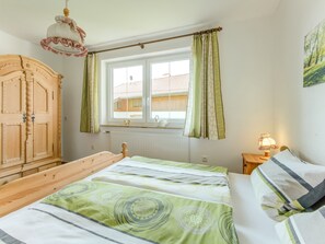 Une chambre à coucher avec un lit en bois, une fenêtre avec des rideaux, un radiateur et une lampe sur une table de chevet.