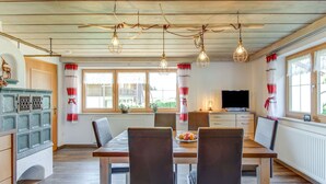 Un comedor con mesa y sillas de madera, televisor y un mueble con adornos.