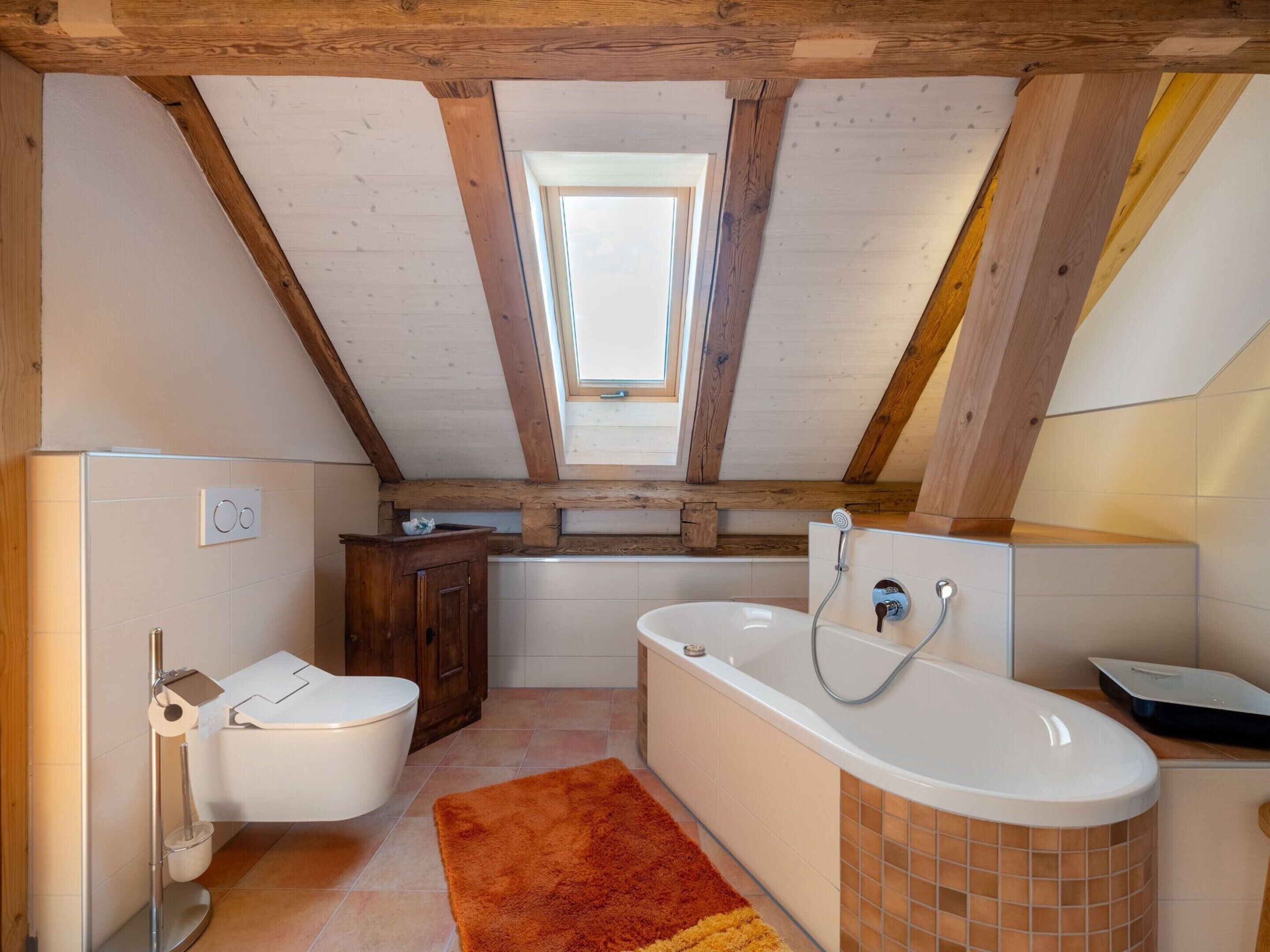 A modern bathroom with a skylight, a bathtub, a toilet, and a vanity.