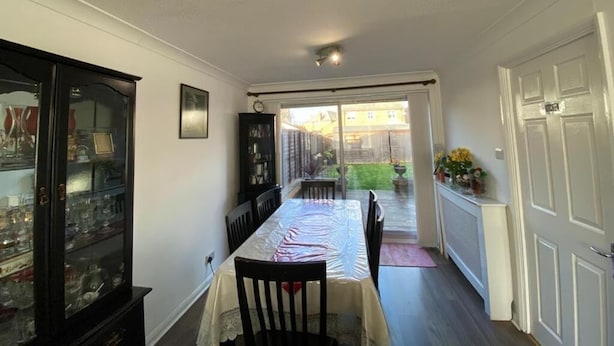 A dining area with a table covered by a protective sheet, a cabinet with glass doors, and a view of a backyard through a sliding door. - Lovely Homes (Aylesbury)
