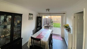 A dining area with a table and chairs, a glass cabinet with dishes, and a view of a backyard through a sliding door. - Lovely Homes (Aylesbury)