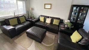 A living room with a sectional sofa, ottoman, and a glass cabinet. - Lovely Homes (Aylesbury)