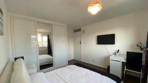 A hotel room with a bed, a desk, a chair, a TV, and a wardrobe. - Lovely Homes (Aylesbury)