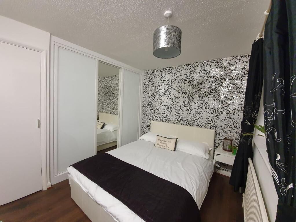 A bedroom with a bed, a nightstand, a mirror, a wardrobe, and a patterned wallpaper.