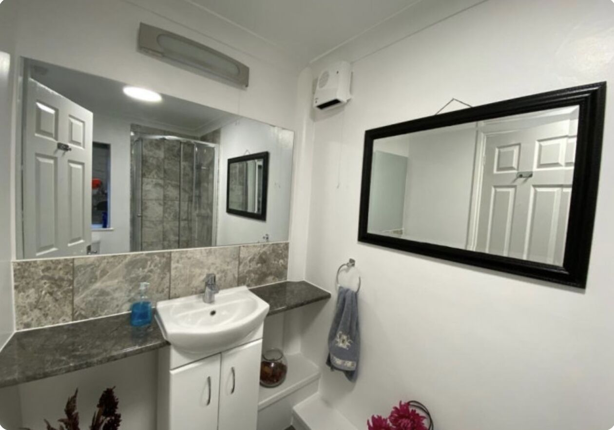 A bathroom with a white sink, a mirror, and a shower area.