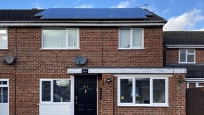 A two-story brick house with a black front door, solar panels on the roof, and a number 217 sign above the door. - Lovely Homes (Aylesbury)