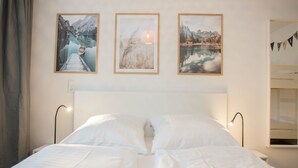 Un lit bien fait, avec du linge de lit blanc, une tête de lit en bois et trois tableaux encadrés accrochés au mur, représentant des paysages pittoresques.