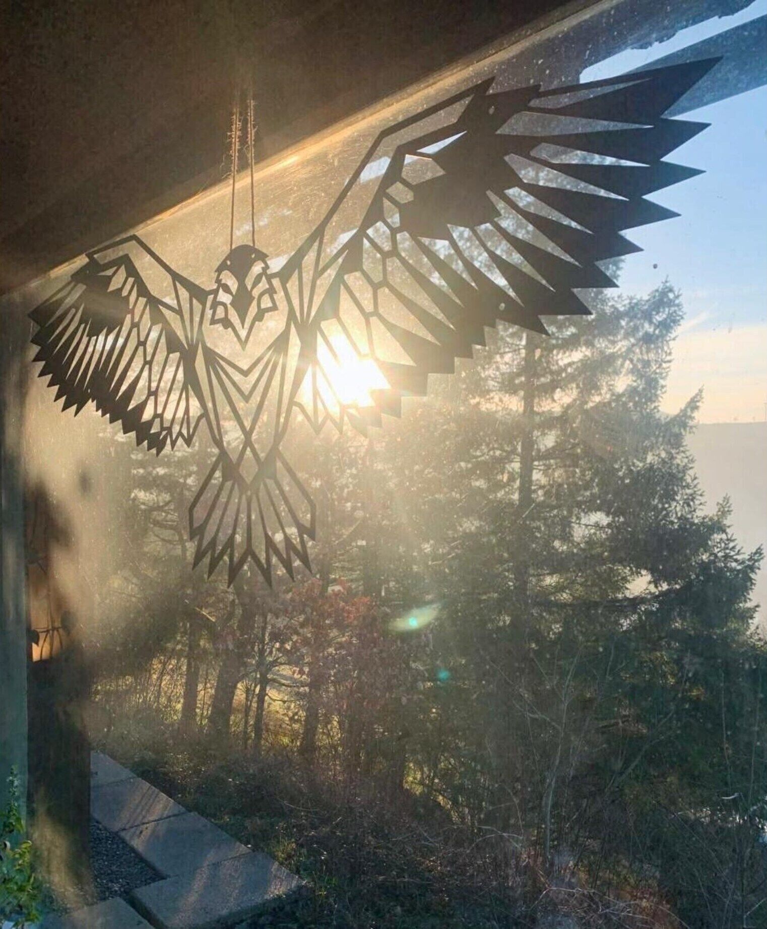 A bird-shaped metal sculpture with wings spread, set against a backdrop of trees and a clear sky.