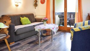 A cozy living room with a sofa, a small table with a vase, and a view of an outdoor area with a table and chairs. - Holiday Flat in Schonau am Konigssee (Schoenau am Koenigssee)