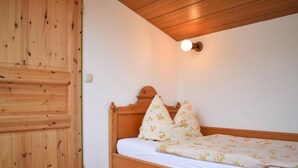 A wooden bed with floral bedding in a room with wooden walls and a sloped ceiling. - Holiday Flat in Schonau am Konigssee (Schoenau am Koenigssee)