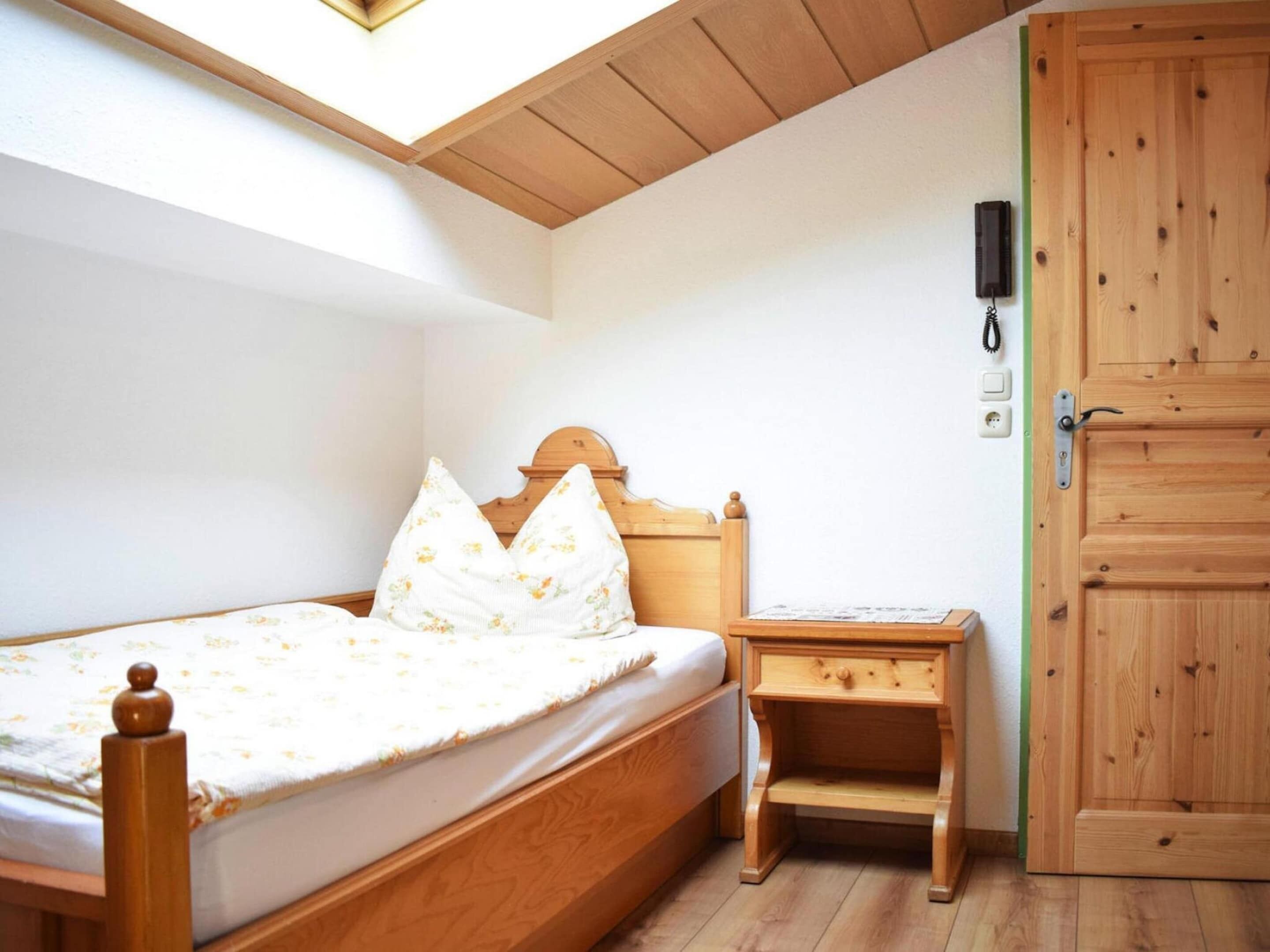 A bedroom with a wooden bed, a nightstand, a wardrobe, and a skylight.